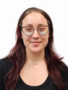 Person with long brown and dark red hair and pointed glasses in a black shirt with a white background