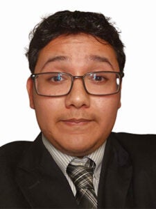 Young Latino man in black suit and yellow plaid tie and white collared shirt with brown glasses and dark hair