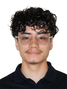 young latino man with wide gold glasses and black curly hair with a black collared shirt in front of a white background