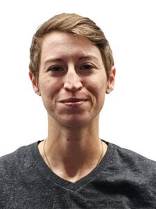 young white woman with blond short hair in grey v-neck shirt smiling in front of a white backdrop
