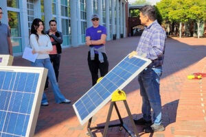group of people standing behind solar panels outside in the shade of the science and technology building
