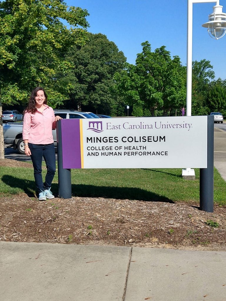 female student next to Minges Coliseum sign