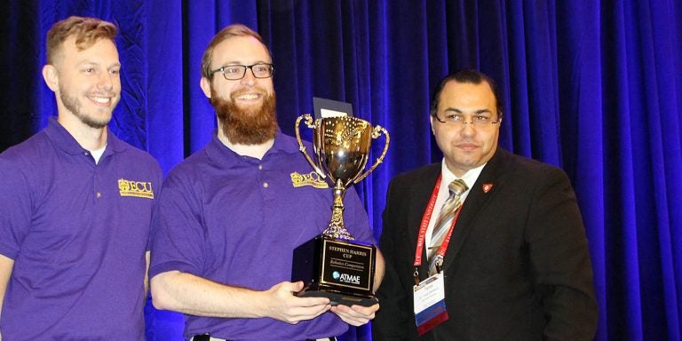 Logan Kelley, left, and Sean Wear, co-leads of the East Carolina University robotics team, receive the Steve Harris Cup for winning the Association of Technology, Management and Applied Engineering robot competition at the organization’s national conference in Charlotte. (Contributed photo)