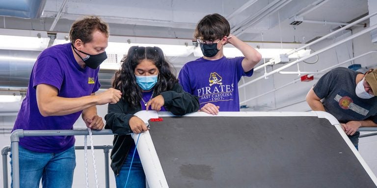 ECU students and Dr. Faete “JT” Filho, left, work on setting up a test of a section of a wave energy desalinization unit at the Coastal Studies Institute. (Photo by John McCord)