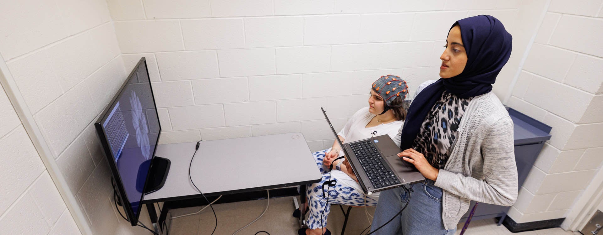 Marwa Antar, a second-year graduate student in biomedical engineering, works with a student wearing a cap that measures electrical activity in the brain. (Photo by Cliff Hollis)