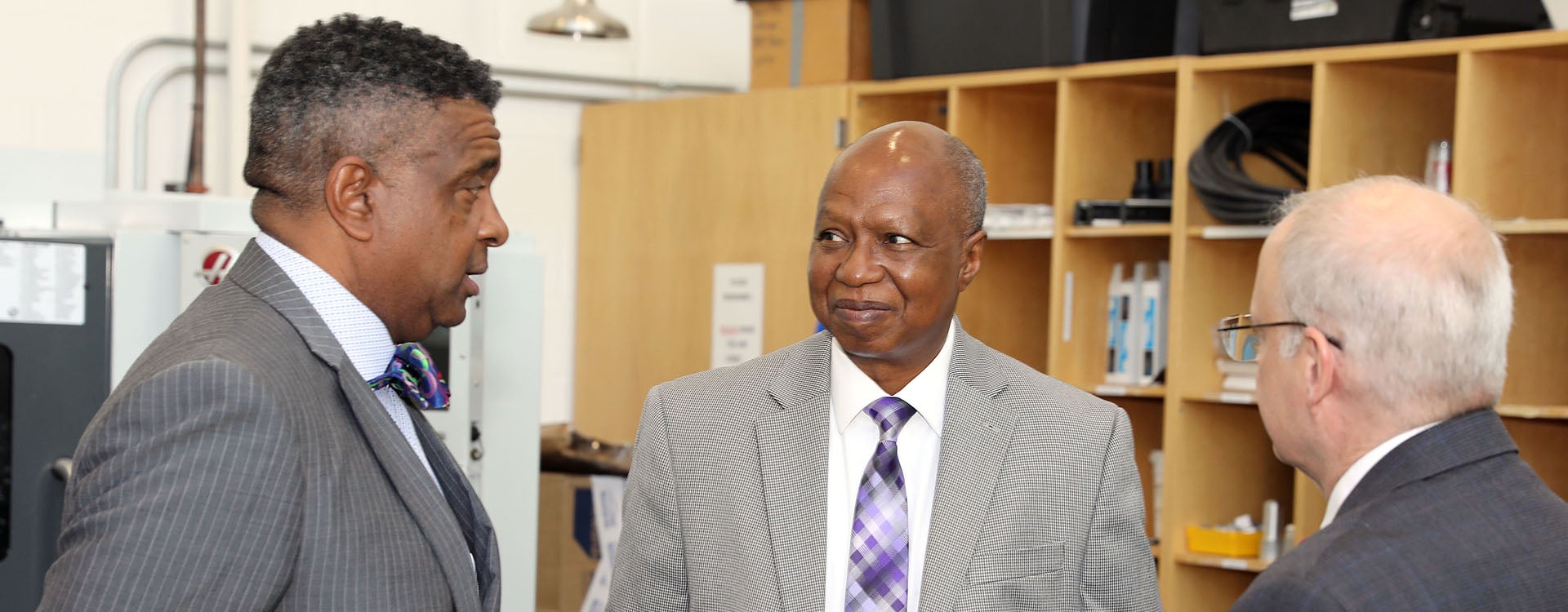 Three men in suits and ties stand and talk in a room.