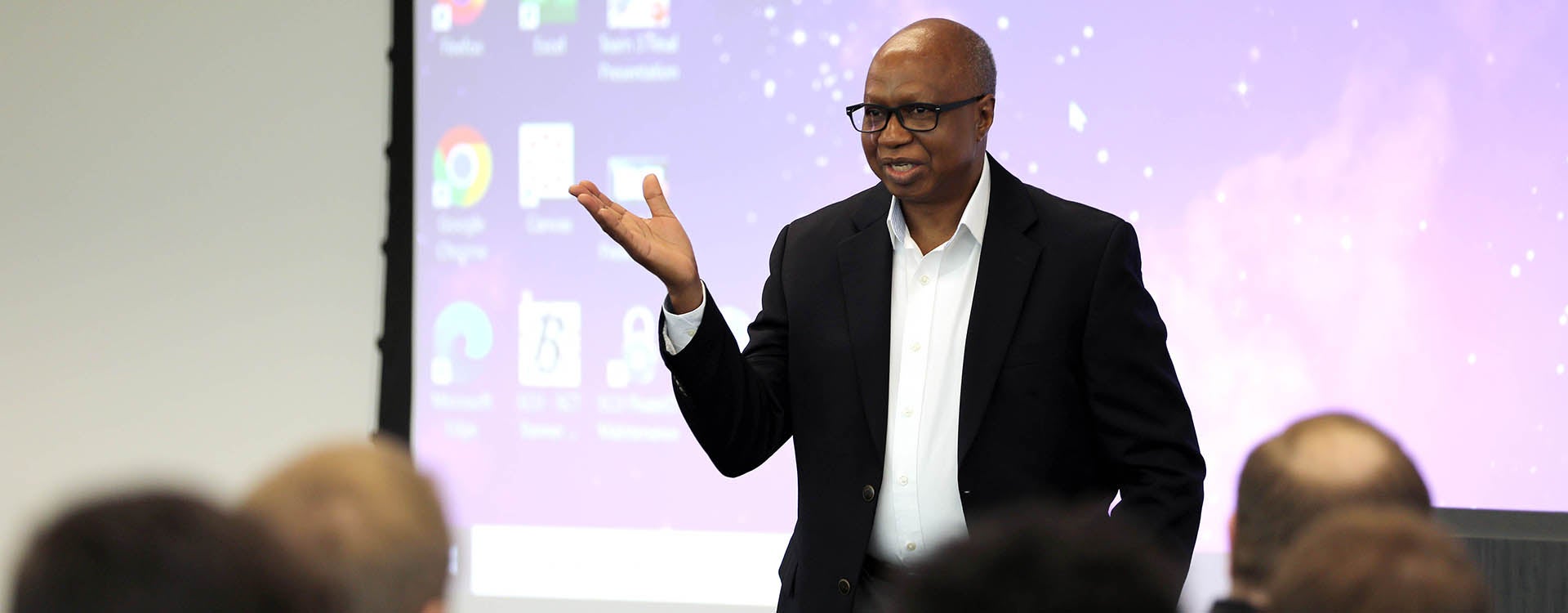 A man in a sport jacket gestures with his hand as he speaks to a group of people.