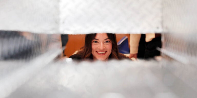 A young woman smiles as she looking through the opening of a metal container.