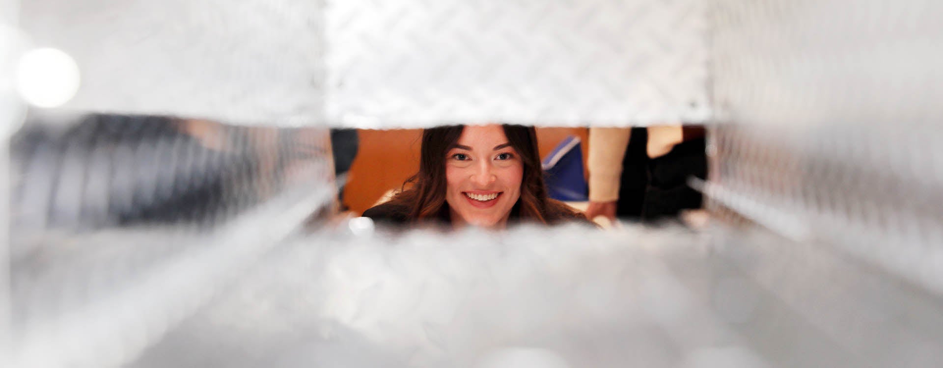 A young woman smiles as she looking through the opening of a metal container.