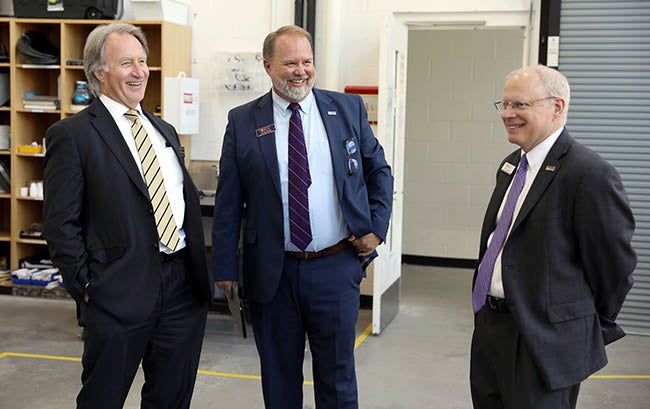 Three men in suits and ties stand and laugh in a large room.