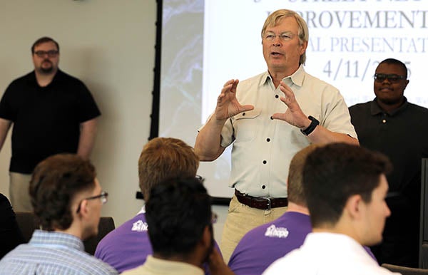 A man gestures with his hands as he speaks in front of a group of people.